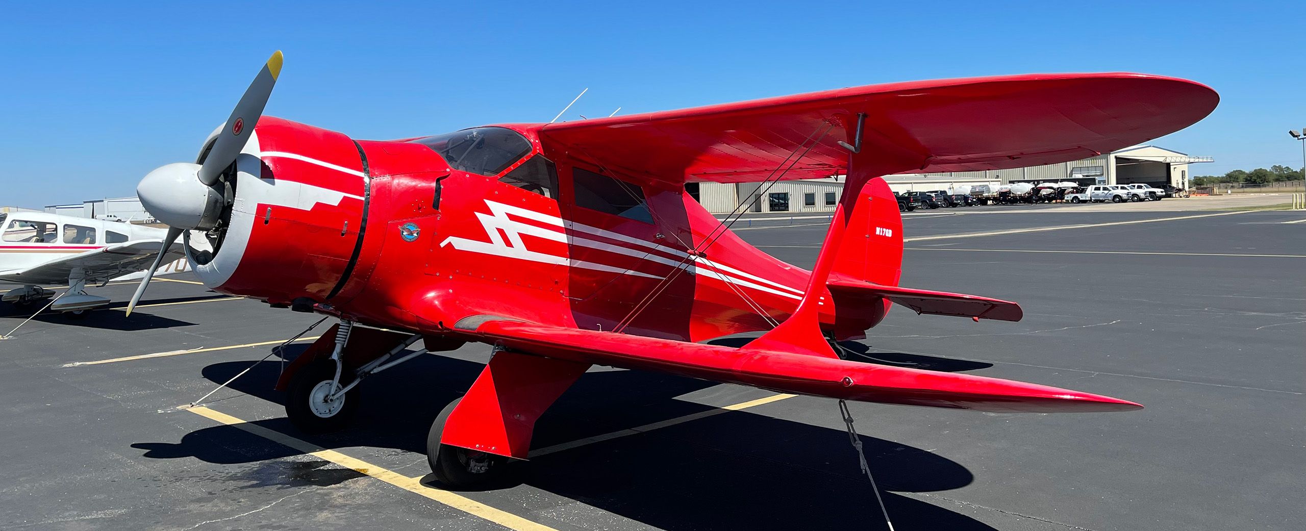 3-quarter-view of a red and white 1944 beech staggerwing sitting on the tarmac. vivid blue sky.