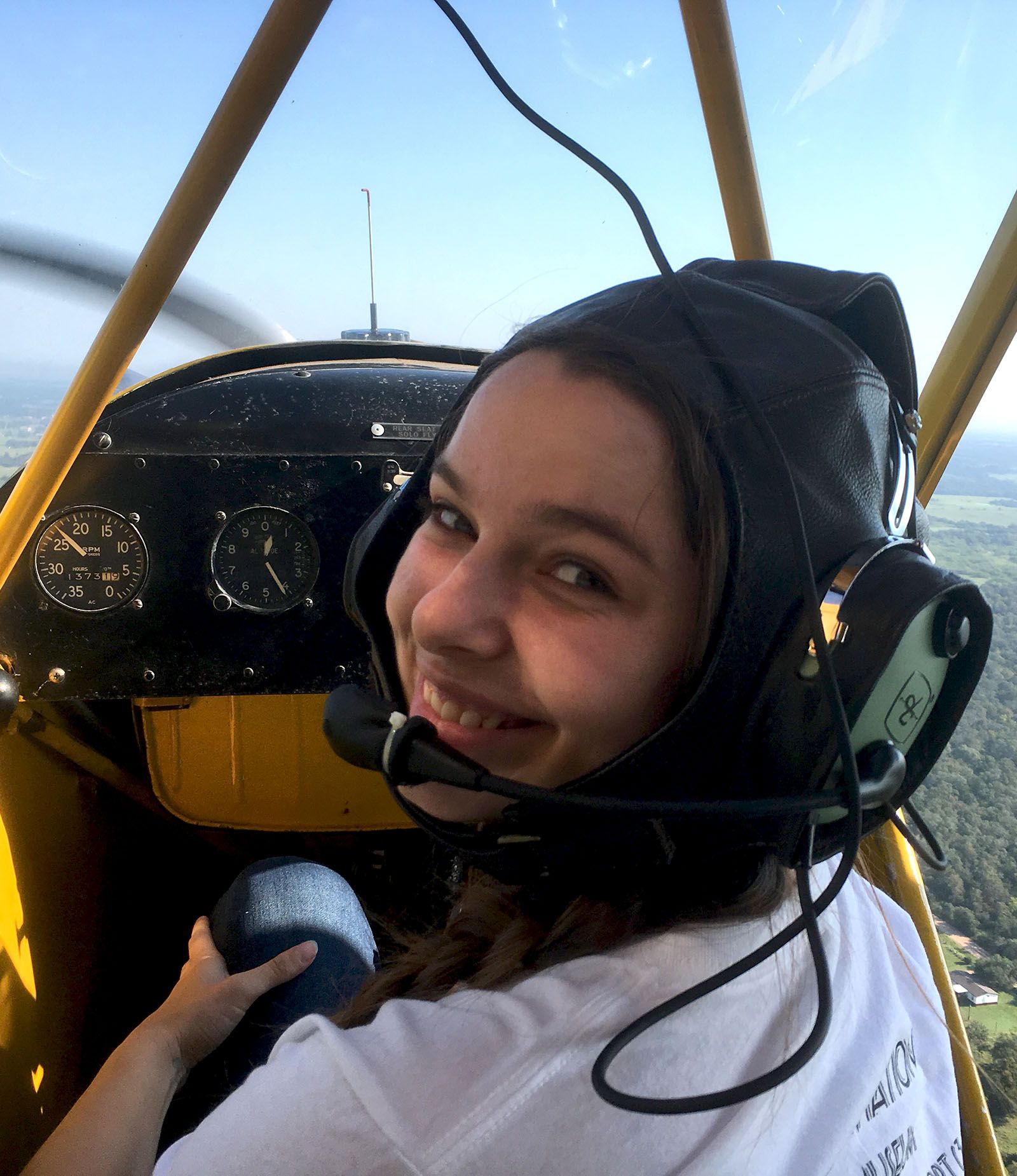 girl in aviator helmet and headset turning to smile at person in back seat of piper cub