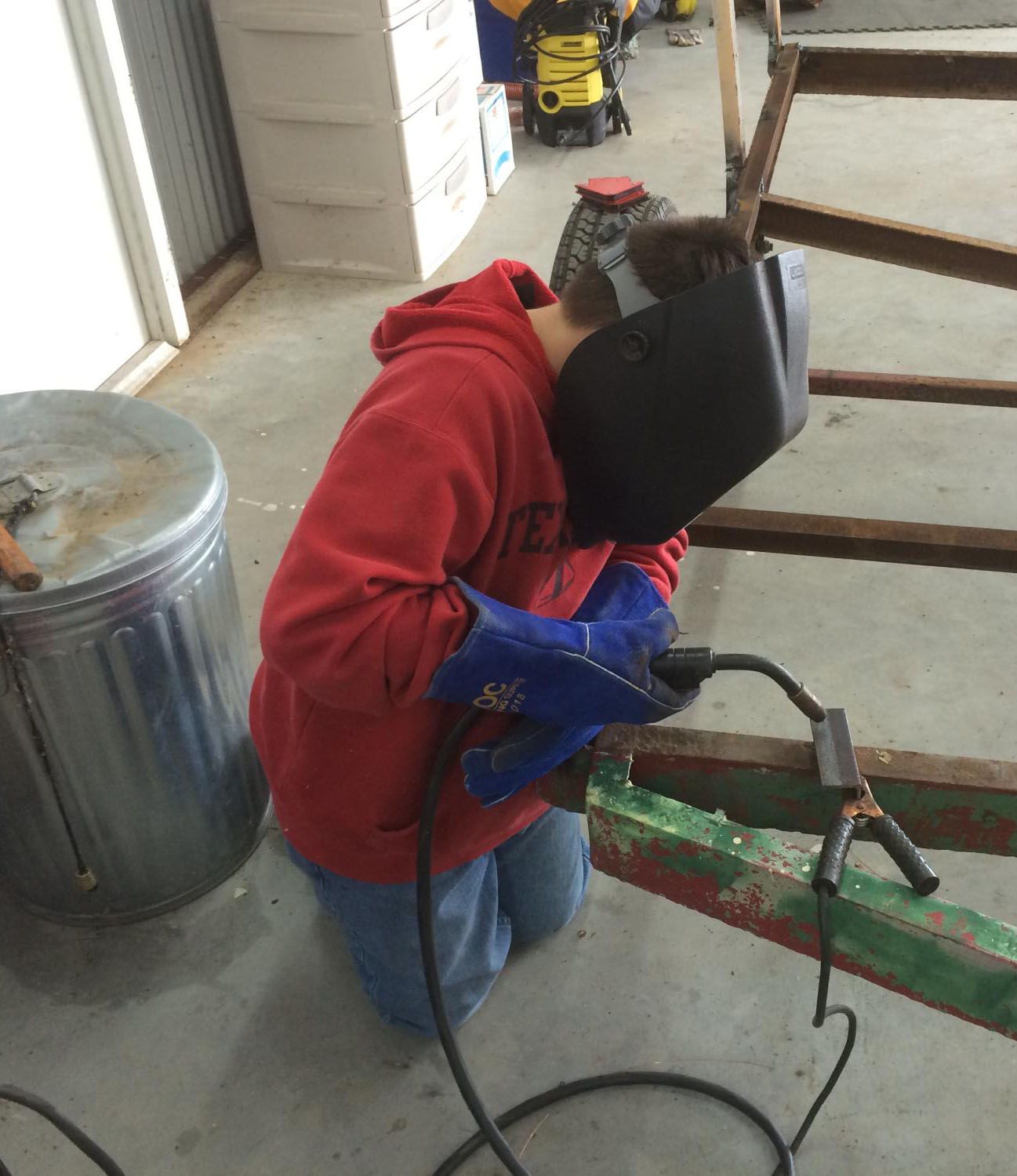 young person in red hoodie and jeans kneeling on the floor welding