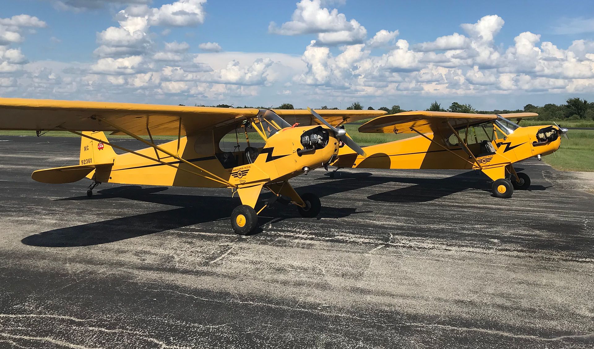 two yellow and black piper cub airplanes side by side on the taxiway