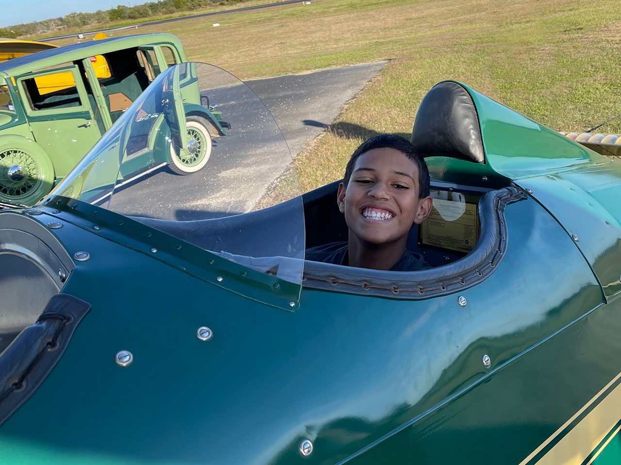 Smiling young latino boy in the cockpit of a green and yellow biplane