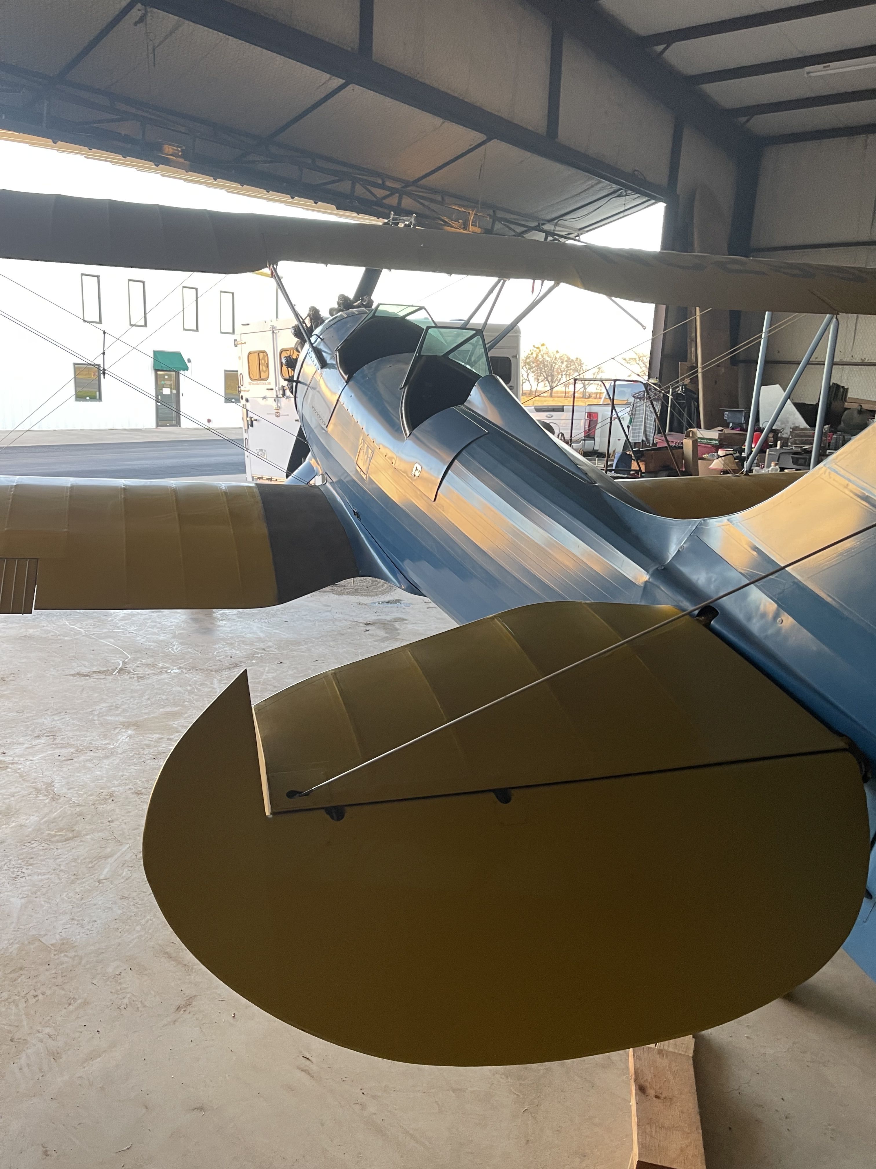 a blue and white rose parrakeet biplane sits at an the airport tiedown.