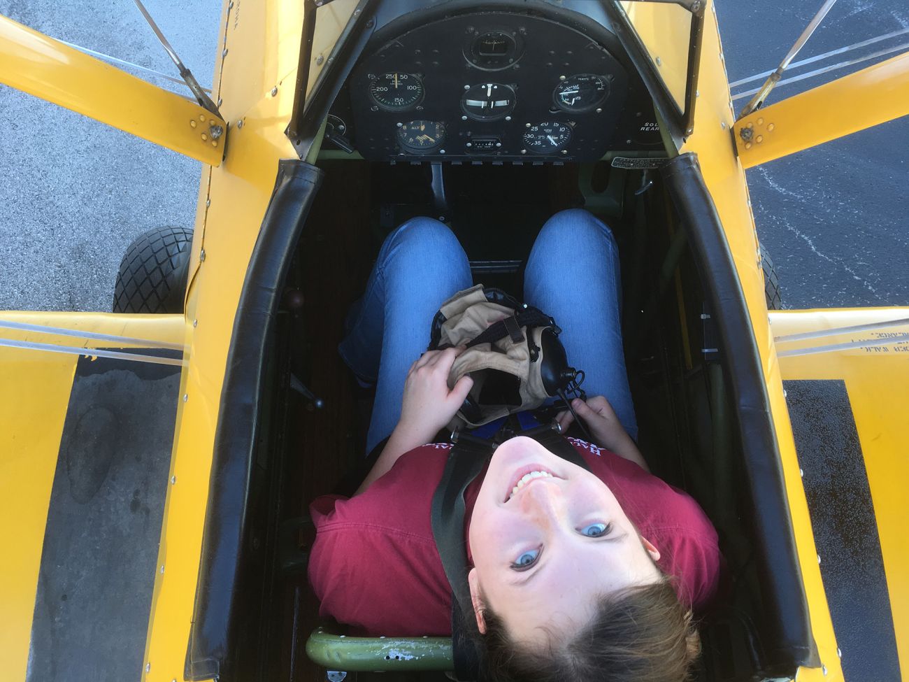 girl in cockpit of piper cub, she is looking up and smiling at the camera which is directly overhead
